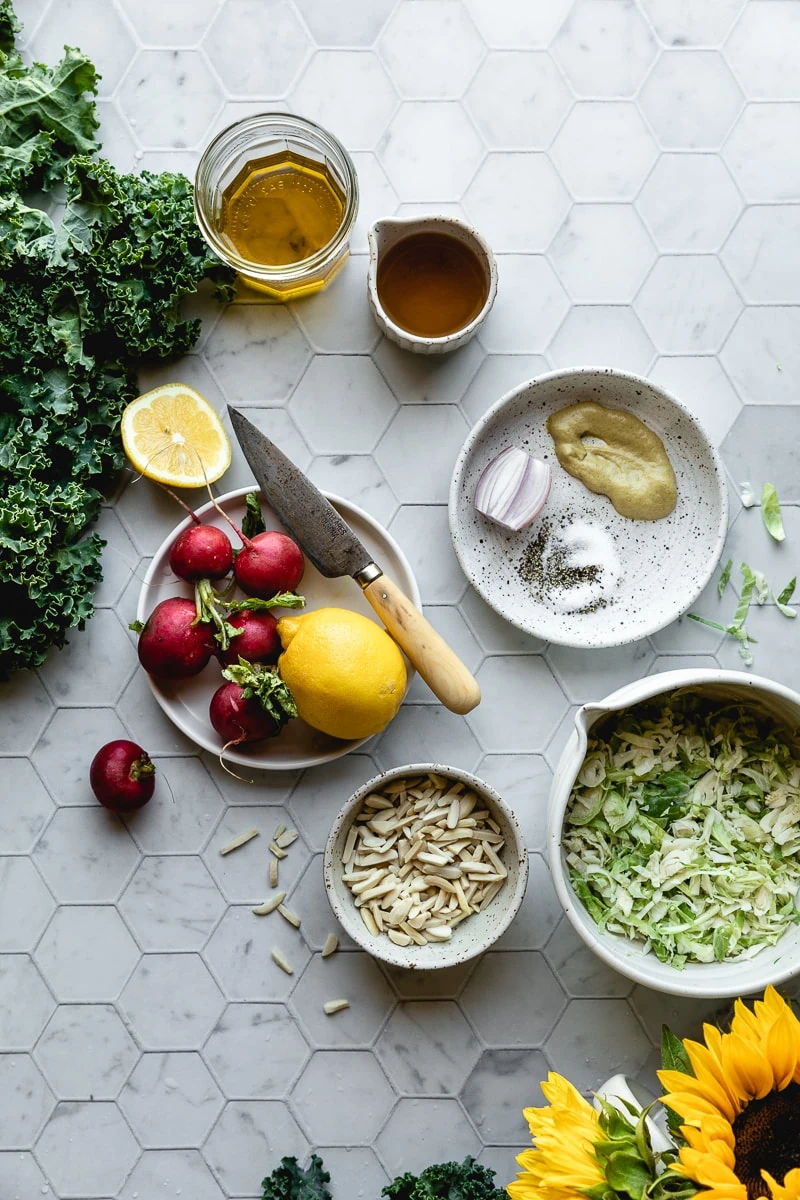 flatlay of radishes, lemon, cabbage and kale plus other ingredients required to make kale crunch salad.