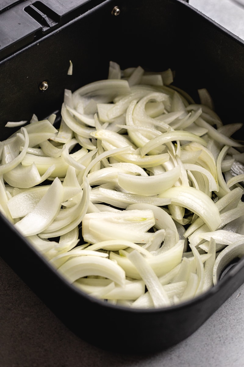 Raw onions in a black air fryer basket.