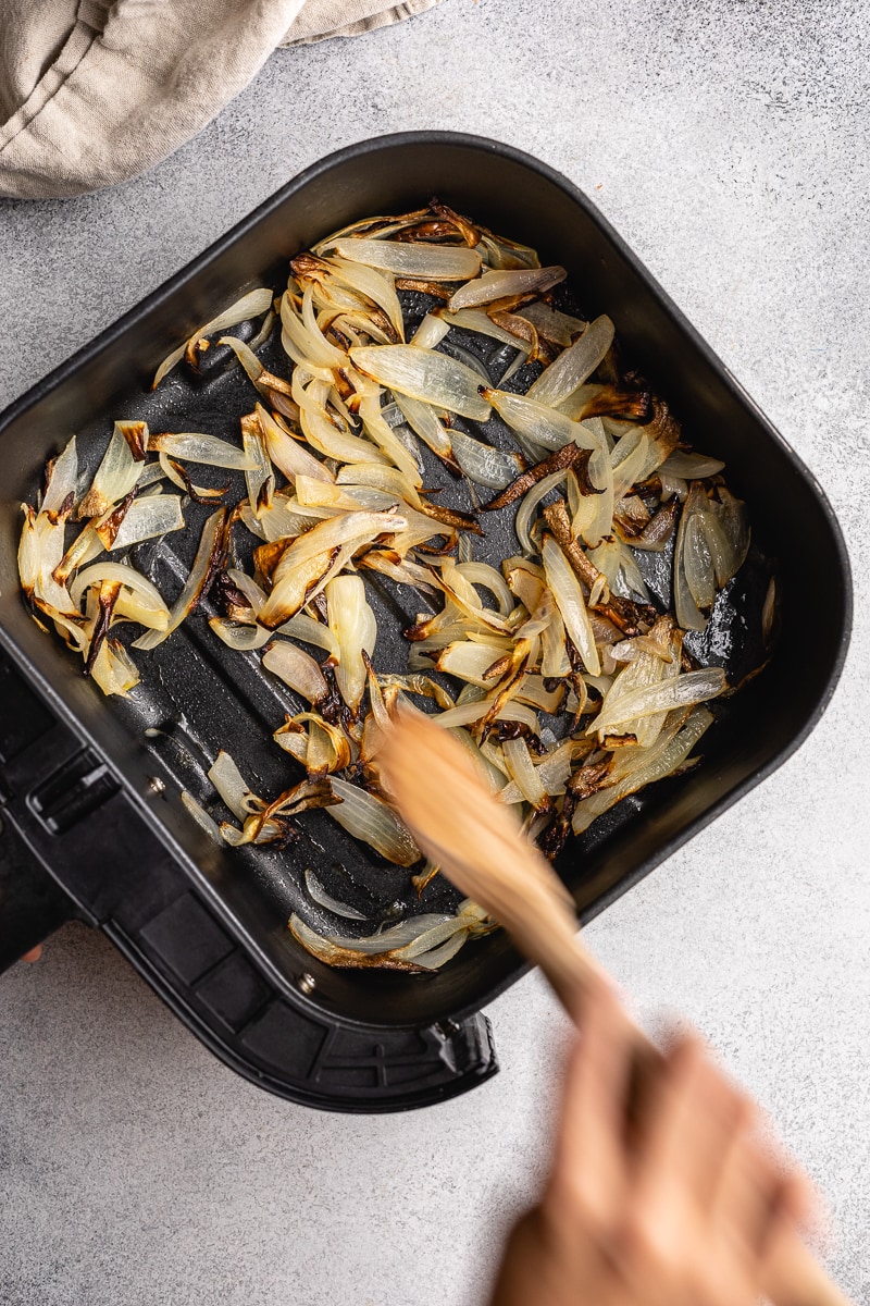 Stirring air fryer onions in a black air fryer basket.