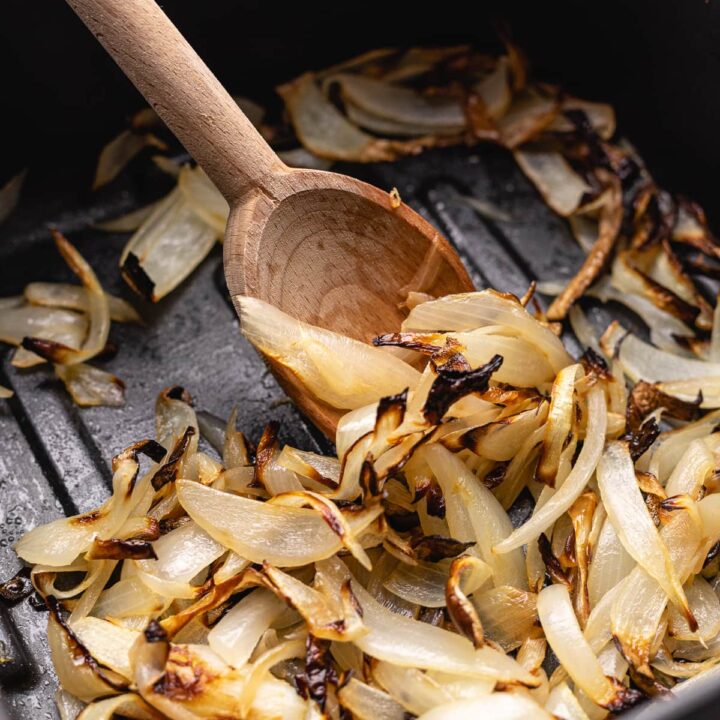 air fryer onions in an air fryer basket being scooped with a wooden spoon.