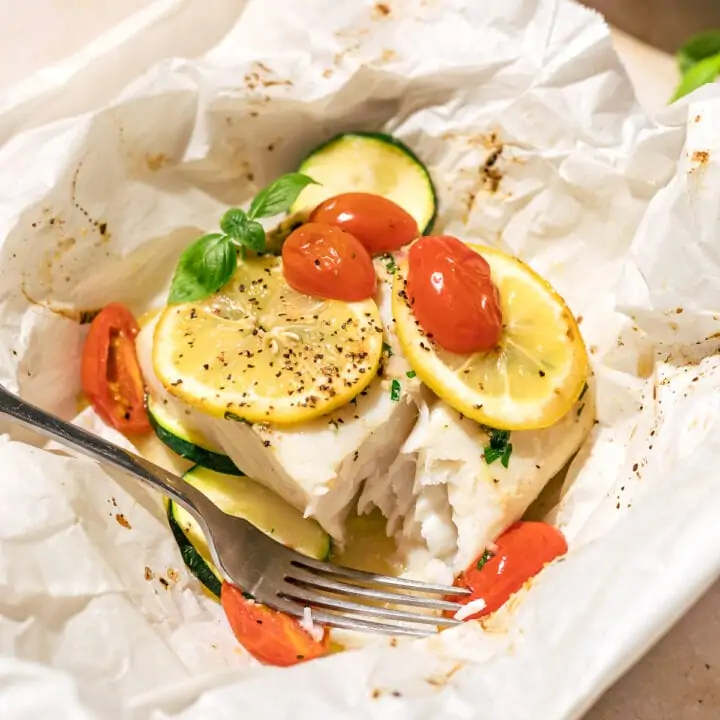 A piece of air fryer halibut en papillote with a fork and basil garnish.