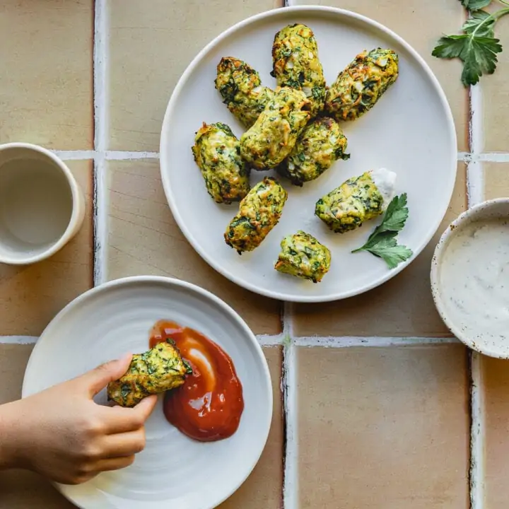 A child's hand dipping an air fryer zucchini in ketchup.