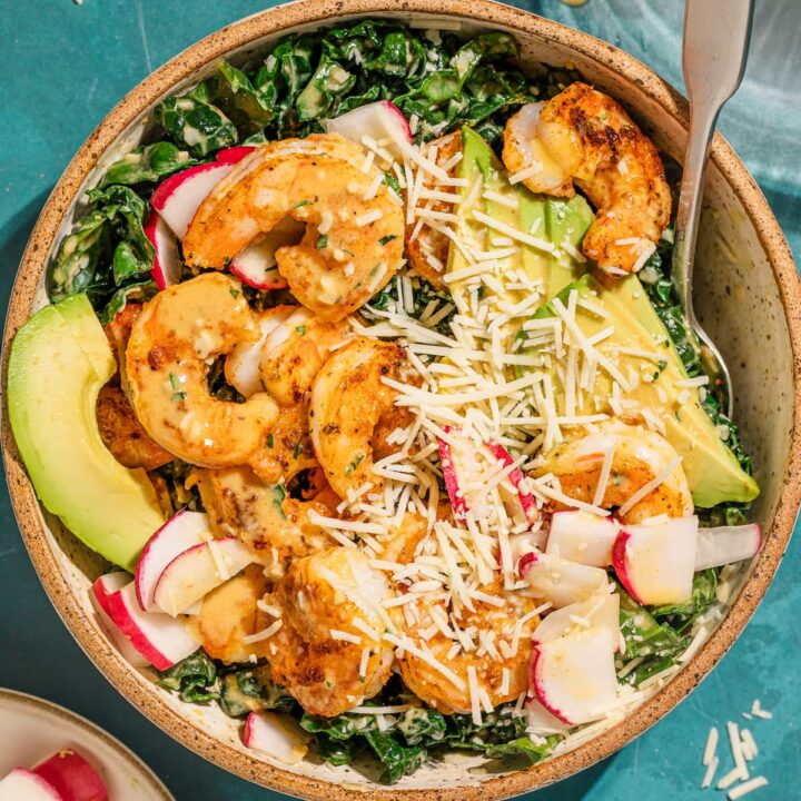 Overhead of a bowl of kale cajun shrimp salad with toppings.