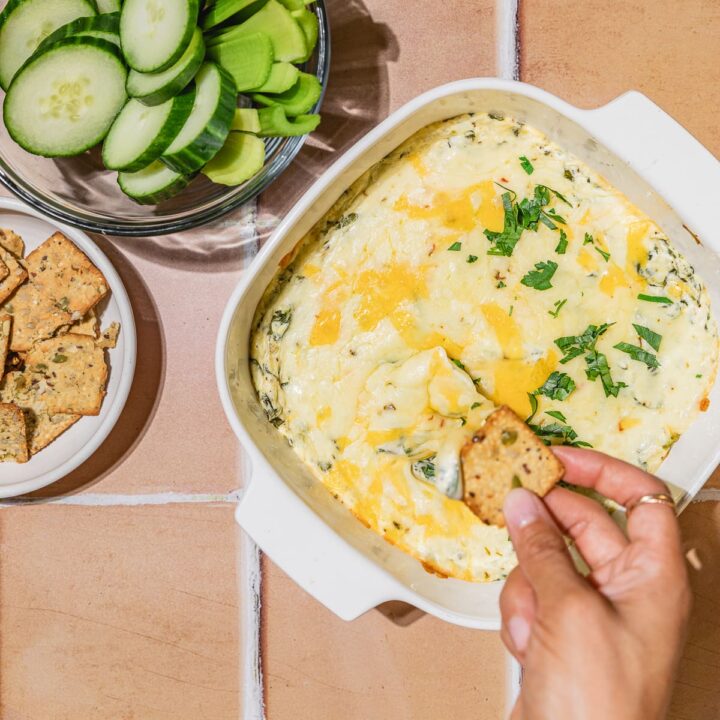 Dipping cracker into baking dish with hot keto spinach dip.