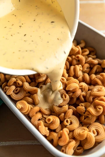 White cheddar sauce being poured onto keto mac and cheese.