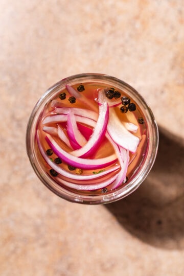 Pickled onions in a jar with peppercorns.