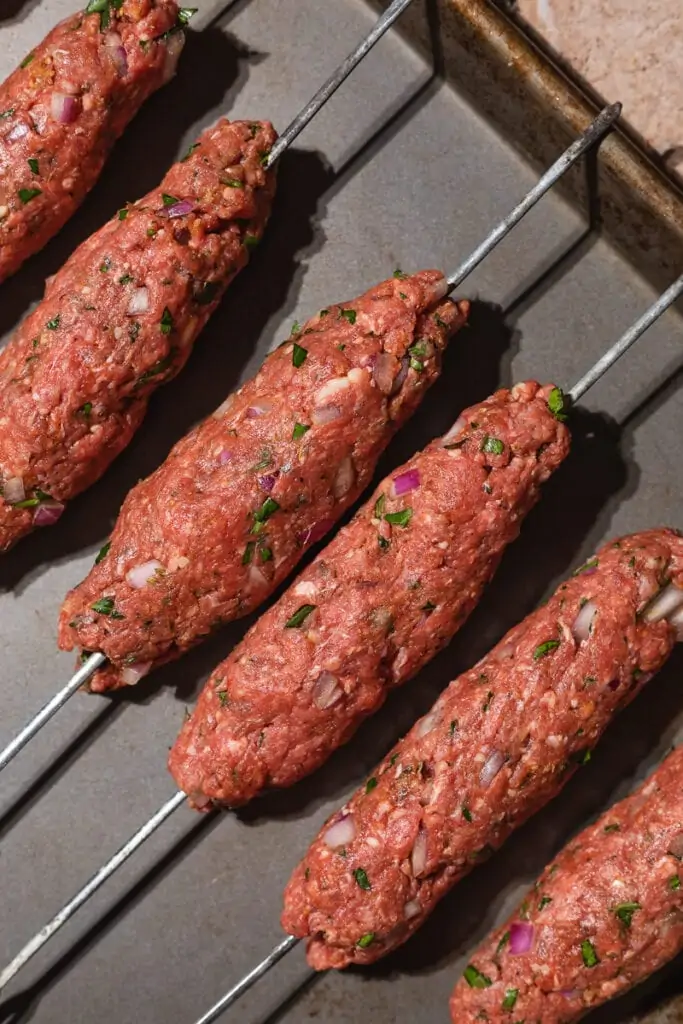 Raw ground beef kebabs on metal skewers.