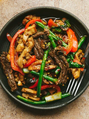 Chicken and steak stir fry on a black dish with a fork.