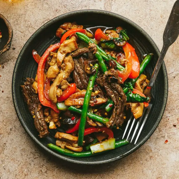 Chicken and steak stir fry on a black dish with a fork.