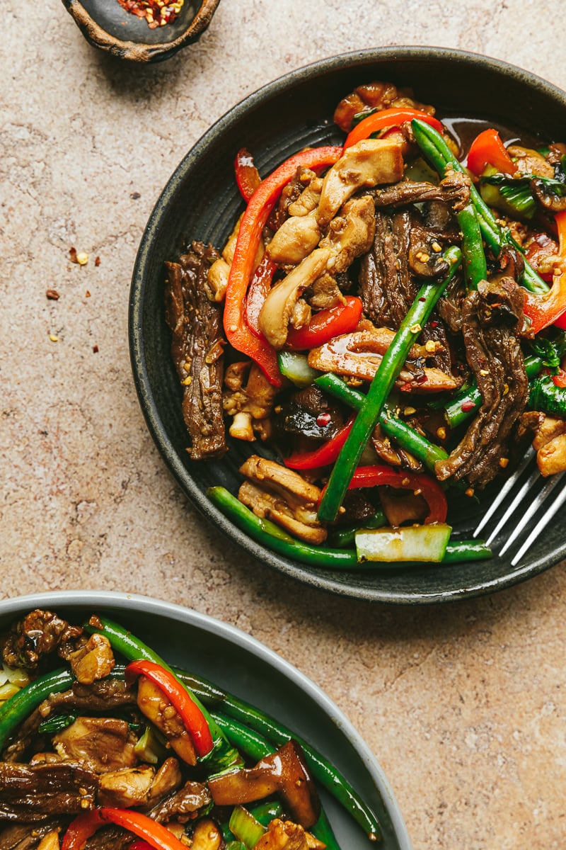 Two plates with chicken and beef stir fry.