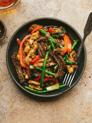 Plate of chicken and steak stir fry on a brown marble surface.