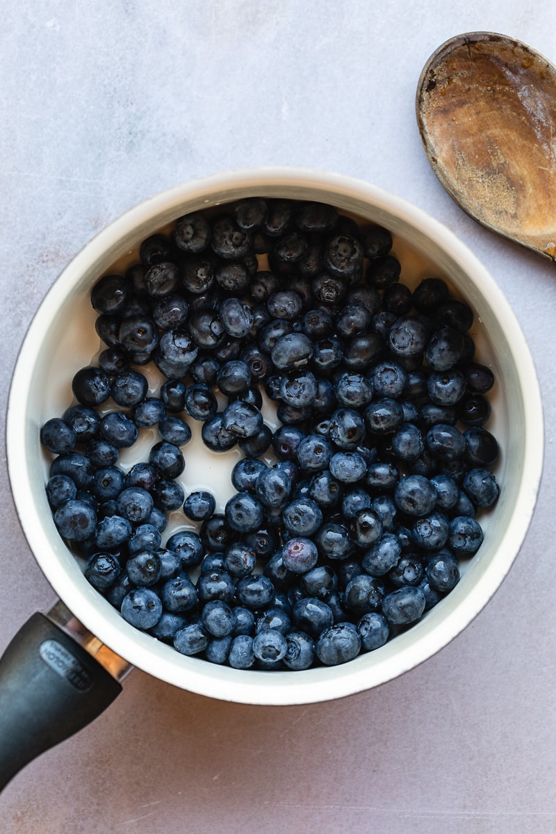 Overhead of fresh blueberries in a saucepan with a wooden spoon.