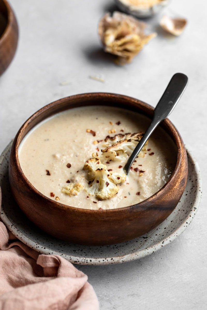 Straight-on shot of creamy keto roasted cauliflower soup in a wooden bowl with a spoon.