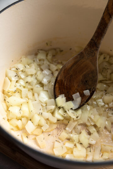 Chopped onions and thyme in a Dutch oven with a wooden spoon.