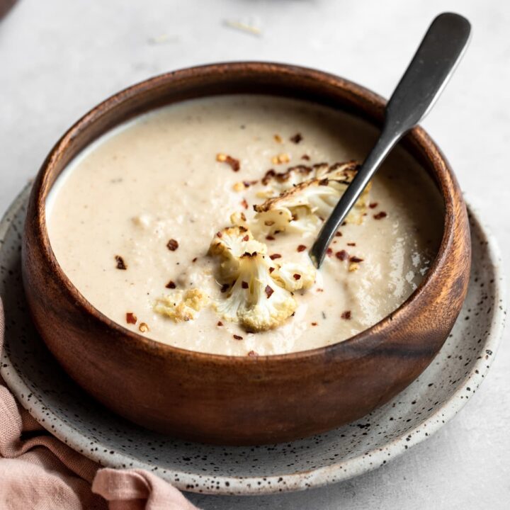 Keto cauliflower soup in a wooden bowl with roasted cauliflower florets on top.