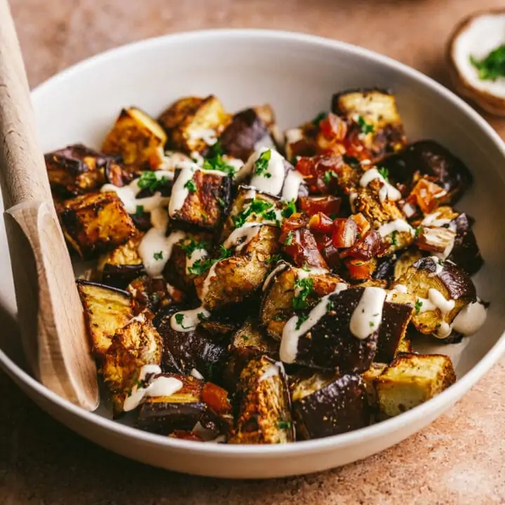 Mediterranean roasted eggplant in a serving bowl with tahini and parsley on top.