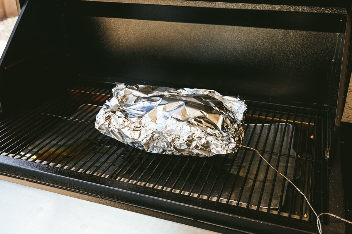 Brisket on a Traeger grill wrapped in aluminum foil.
