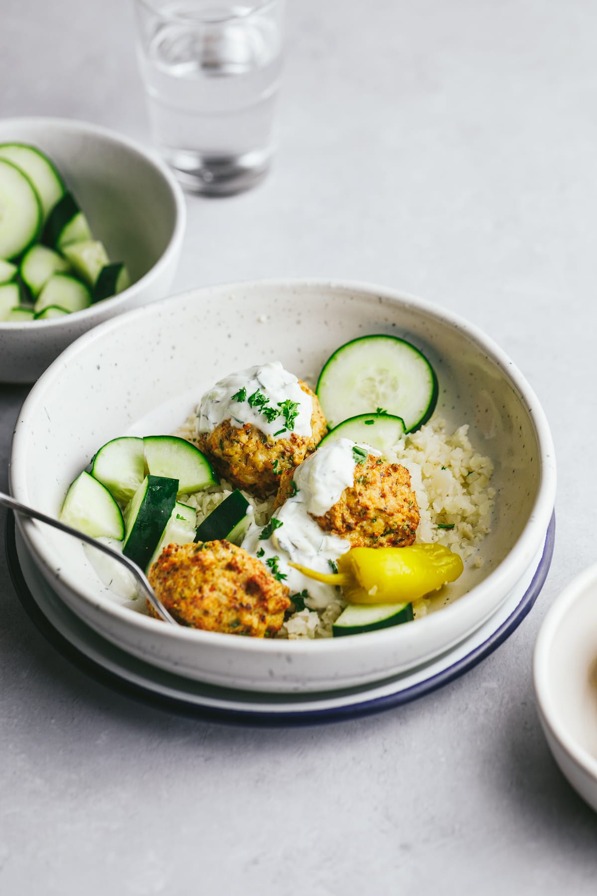 Greek chicken meatballs in a bowl with cauli rice, cucumbers and tzaziki.
