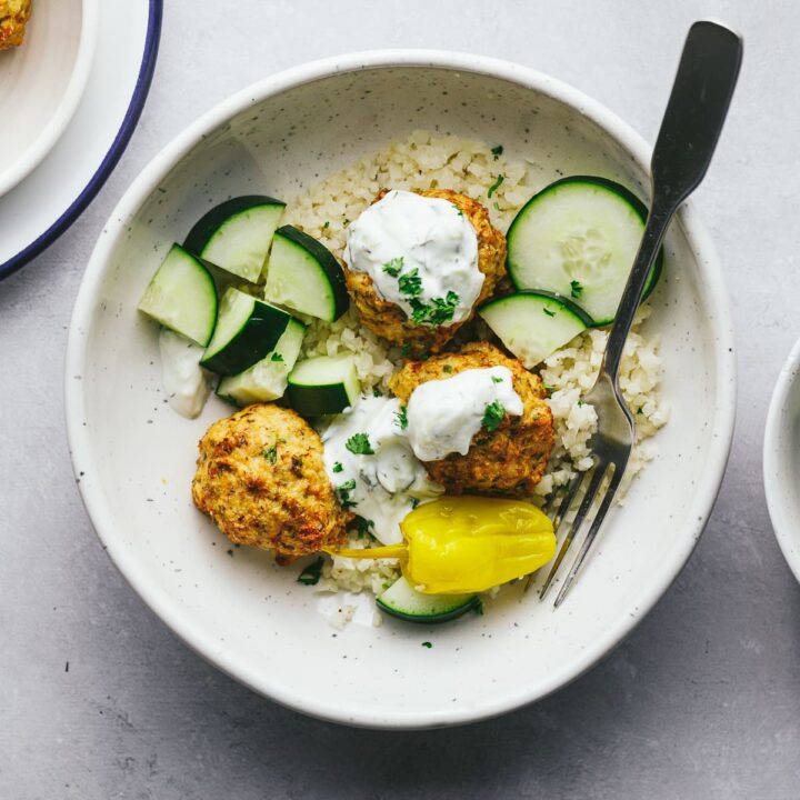 Air fryer chicken meatballs in a bowl with cucumbers and tzaziki.