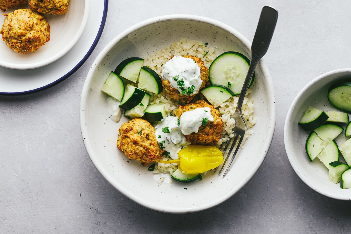 Keto Greek chicken meatballs in a bowl with cucumbers and tzaziki.