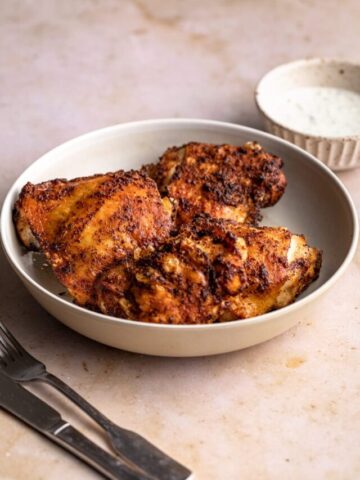 Air fryer chicken thighs on a plate with dipping sauce in a dish.