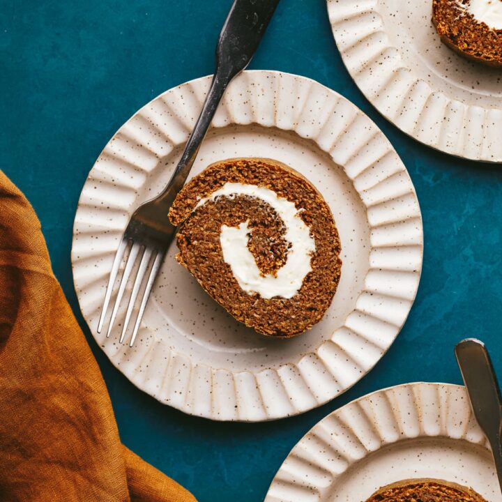 A slice of keto pumpkin roll on a scalloped plate with a fork.