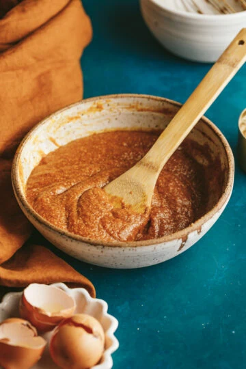 Pumpkin cake batter in a mixing bowl with wooden spatula.