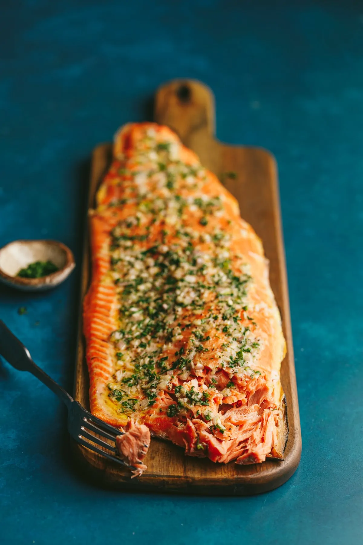 A whole grilled salmon fillet on a wooden cutting board with a fork.