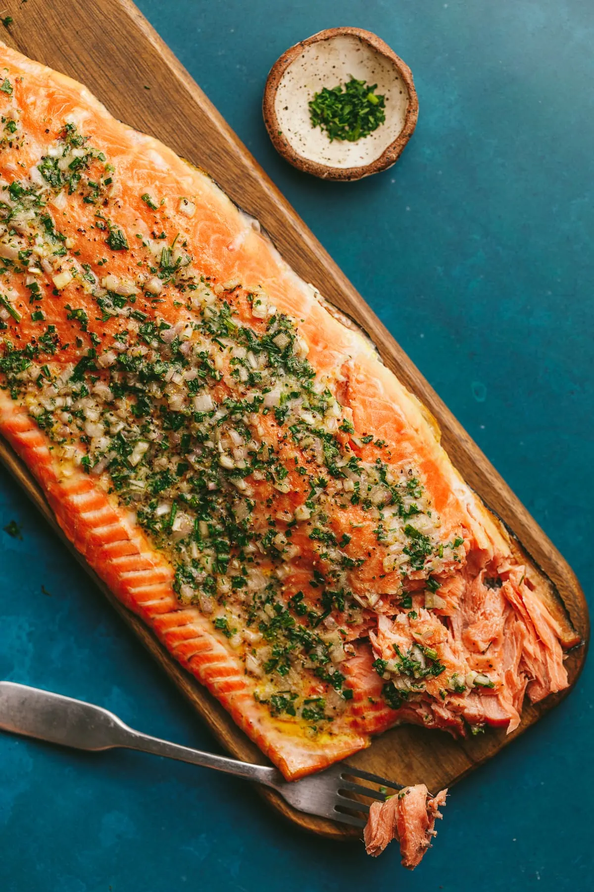 A salmon fillet on a wooden cutting board on a teal backdrop.