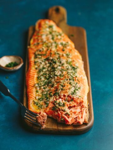 A whole grilled salmon fillet on a wooden cutting board with a fork.