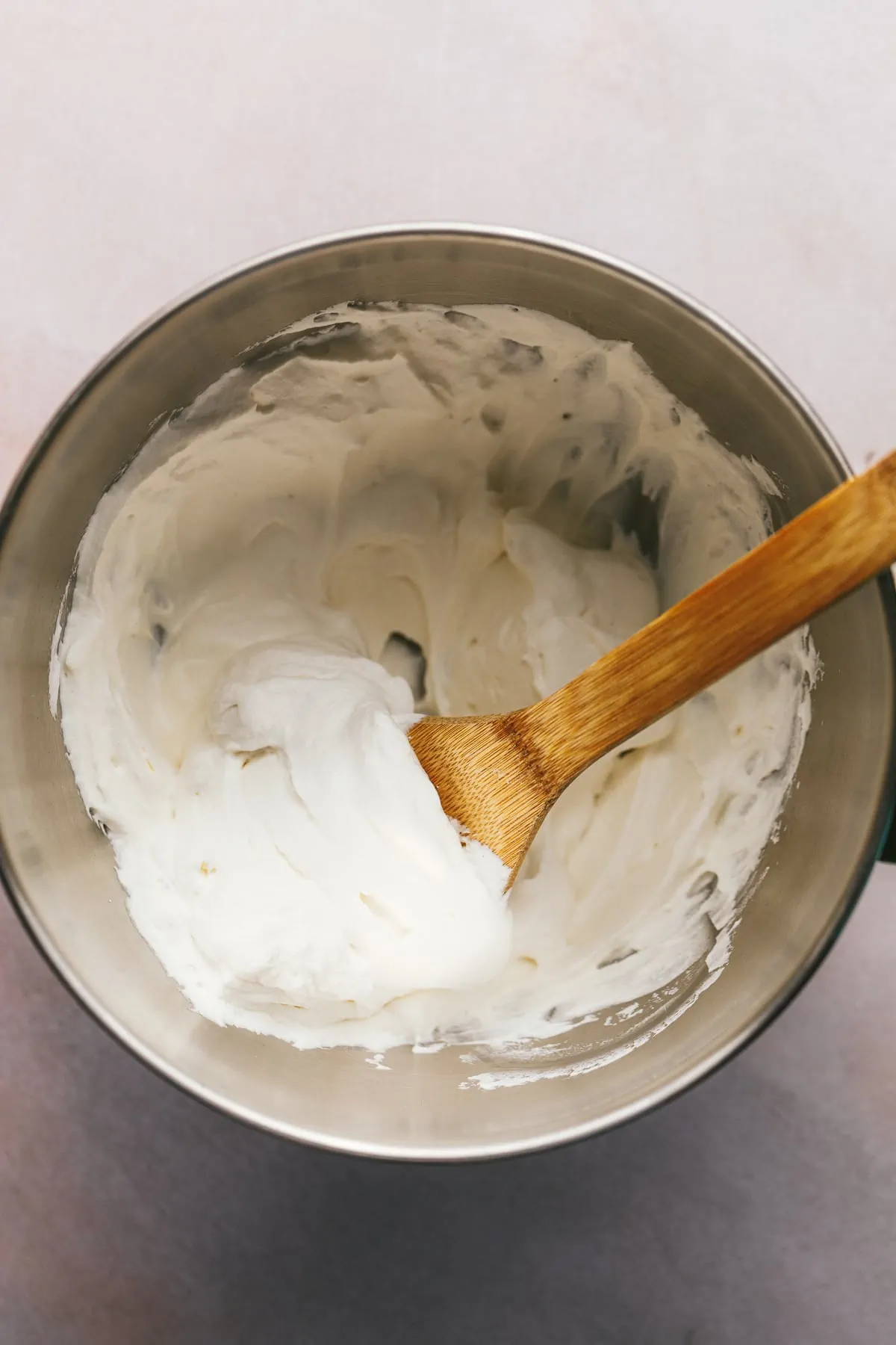 Sugar free whipped cream in a large mixing bowl with a wooden spoon.