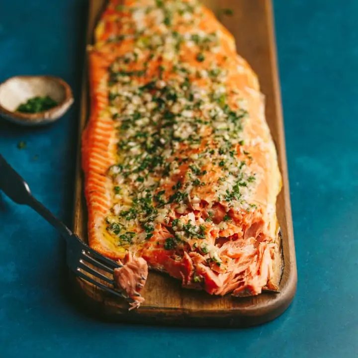 A grilled salmon fillet on a wood cutting board with a fork.