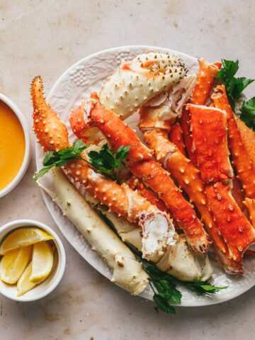 King crab legs on a white platter with spicy bearnaise sauce in a dish on the side.