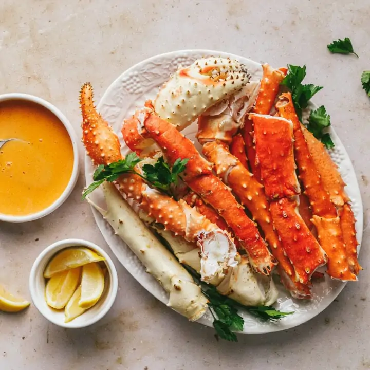 King crab legs on a white platter with spicy bearnaise sauce in a dish on the side.