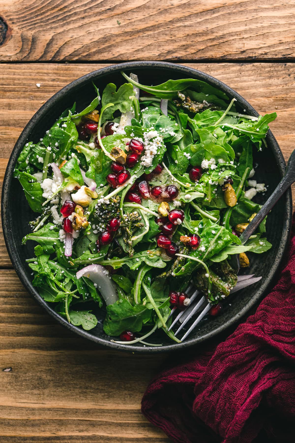 Pomegranate and feta salad with roasted broccolini in a black dish.