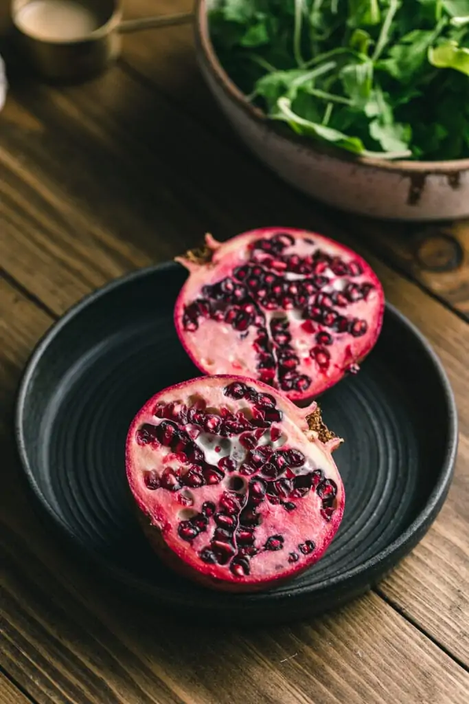 Pomegranate on a black dish on a wood table.