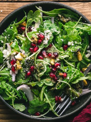 pomegranate and feta salad with roasted broccolini in a black dish.