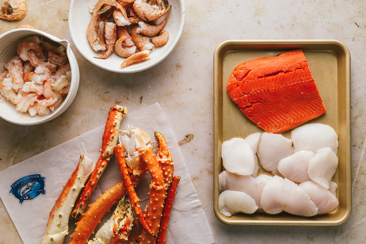 Flat lay of spot shrimp, salmon, halibut cheeks and crab legs for seafood platter recipe.