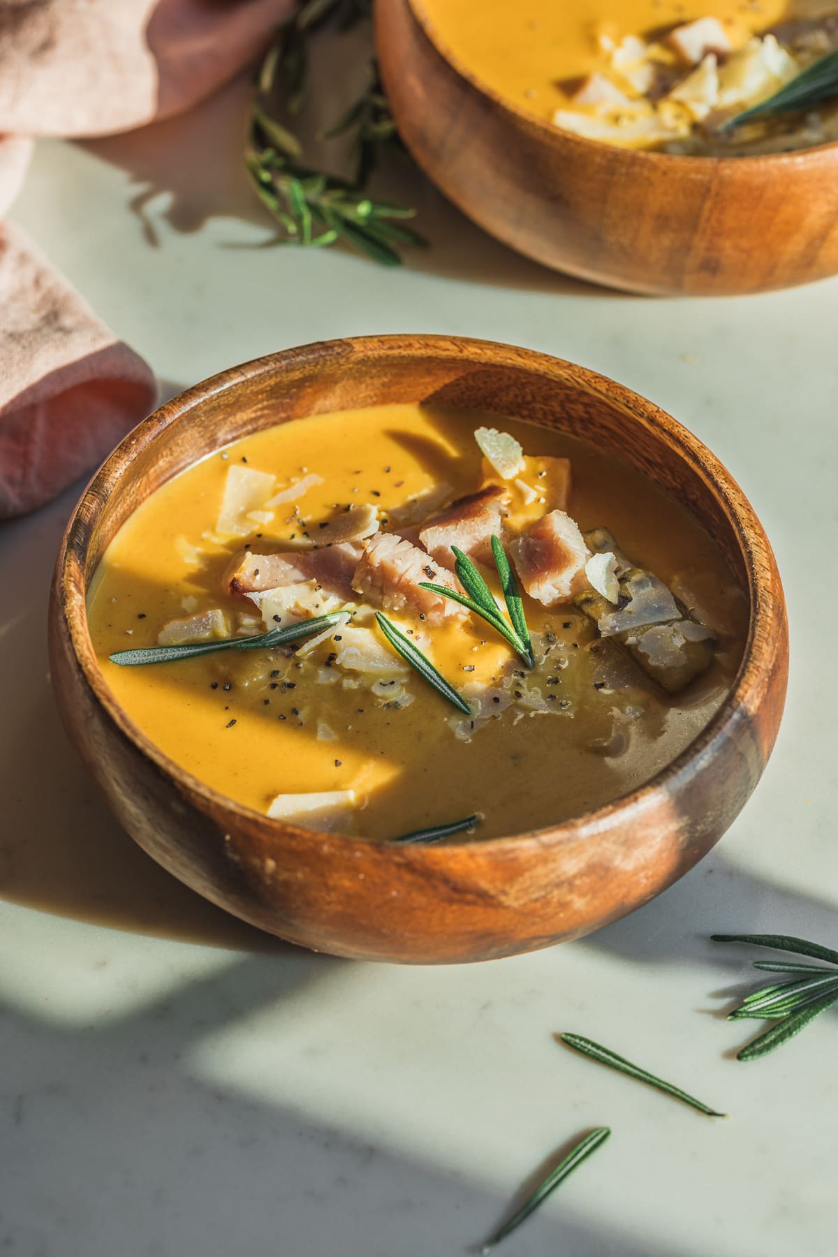 A wooden bowl of butternut squash and carrot soup with chunks of ham and parmesan.