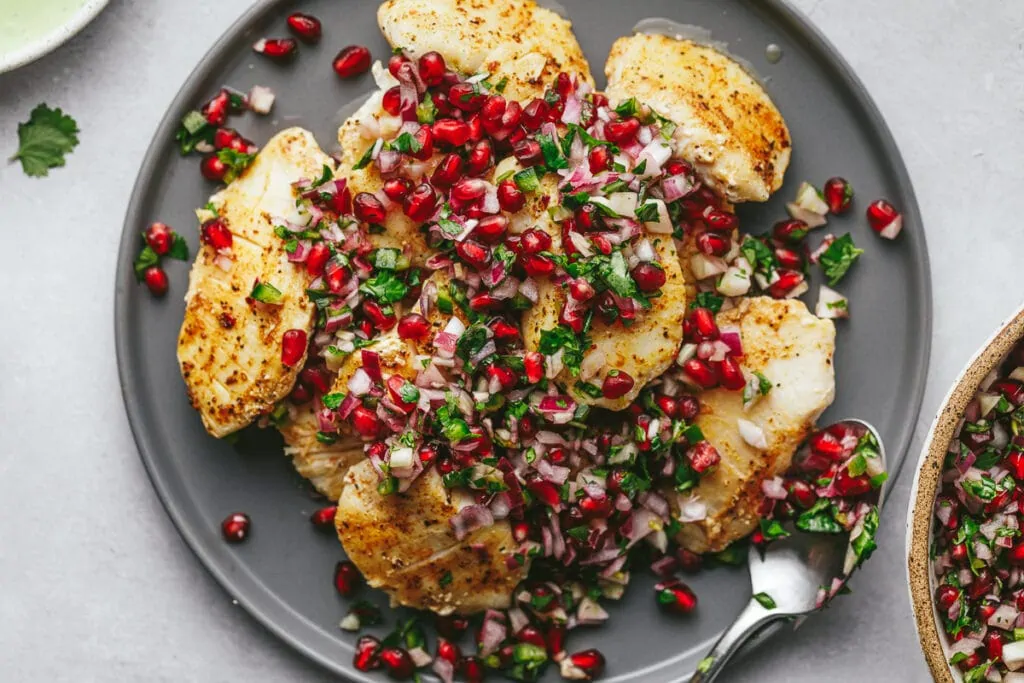 Halibut cheeks with pomegranate salsa on a gray platter.