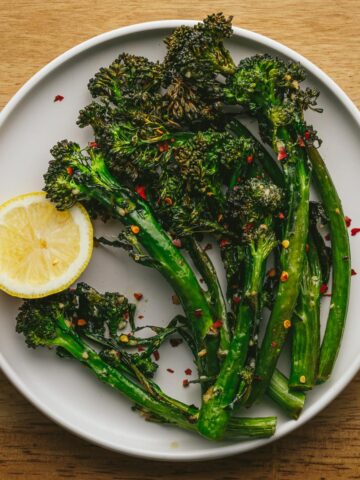 Air fryer broccolini with red pepper flakes on a white plate and wood backdrop.