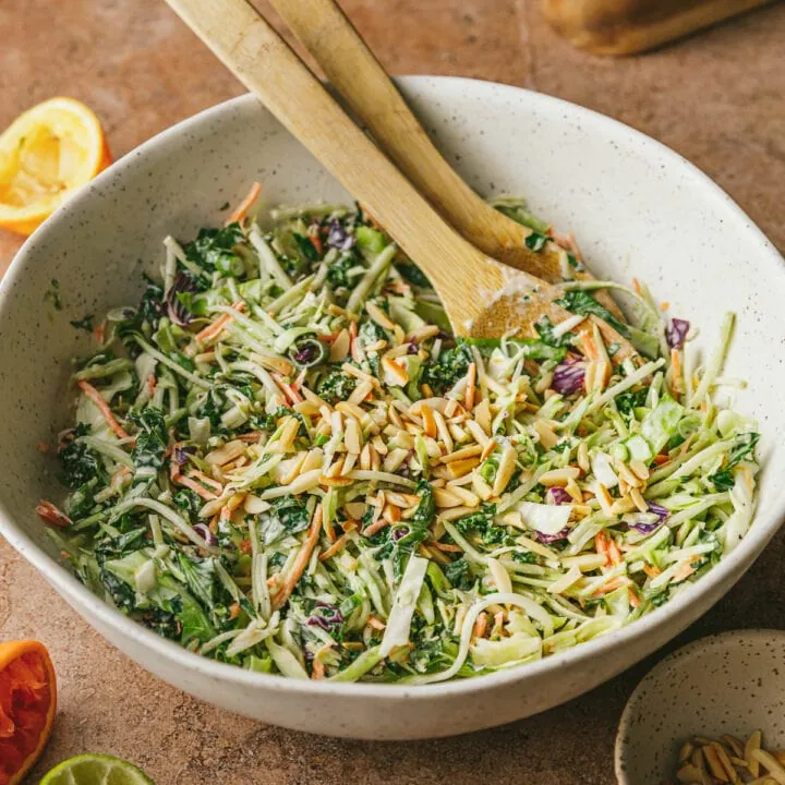 Citrus slaw in a white bowl with serving spoons.