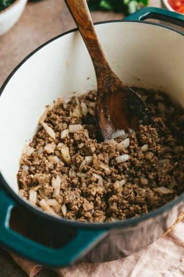 Ground beef and onions in a French oven with a wooden spoon.