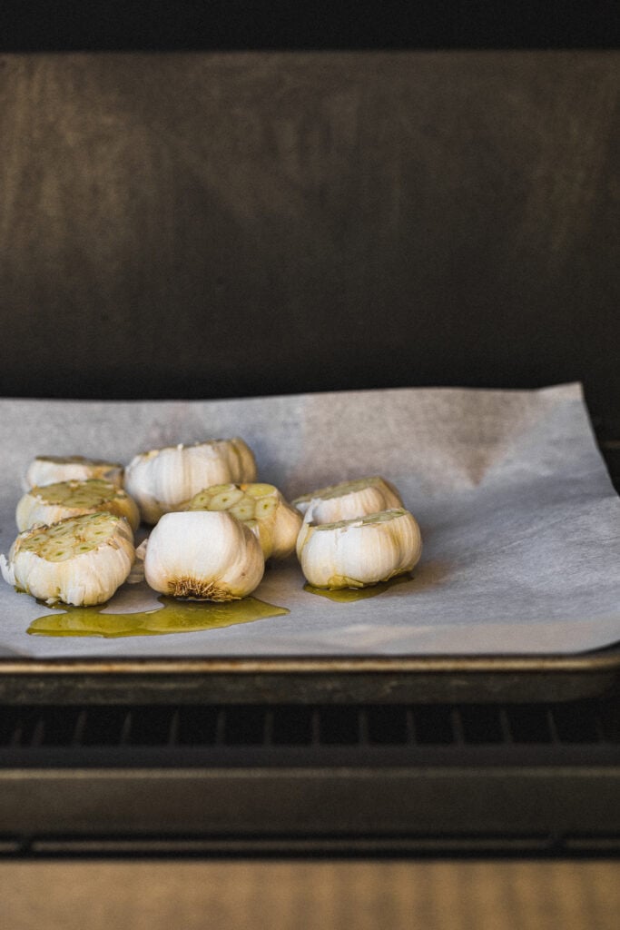 Garlic cloves on a baking sheet in the Traeger grill.