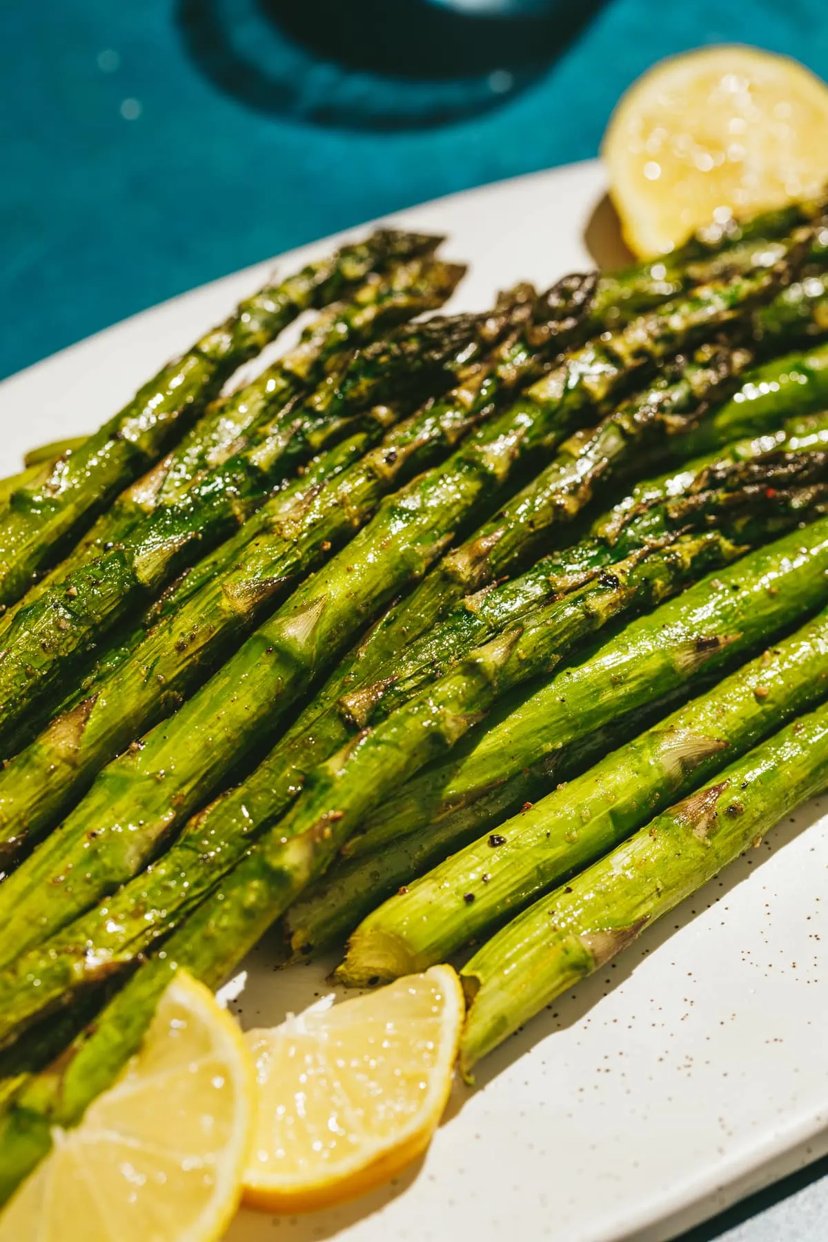 Traeger smoked asparagus on a white plate with lemon slices.