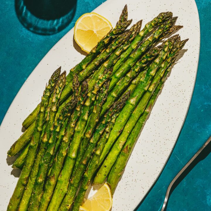 Traeger smoked asparagus on a white platter with a fork.