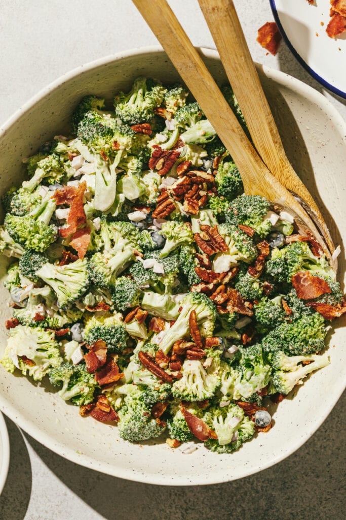Broccoli crunch salad in a serving bowl with wooden spoons.
