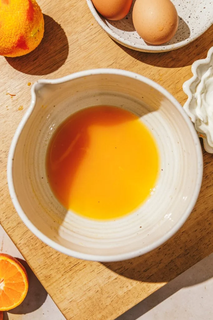 Orange juice in a bowl on a cutting board.