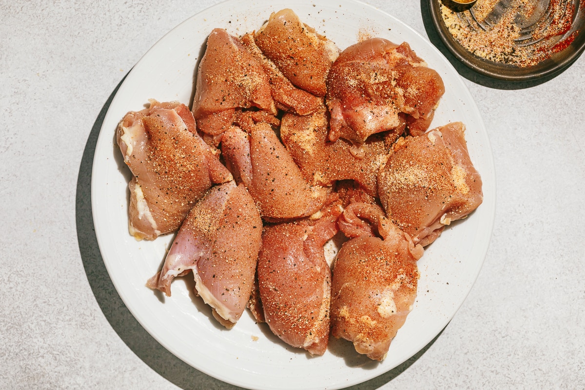 Raw chicken thighs on a white plate with seasoning.