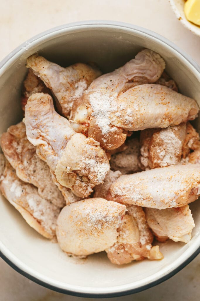 Tossing chicken wings with seasonings in a bowl.